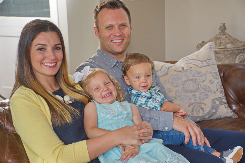 Wife, husband, son and daughter smile at the camera while sitting on their couch.