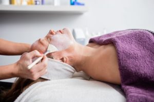 Woman lying down and getting facial treatment brushed on her skin.