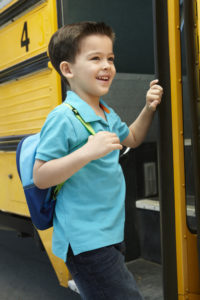 Young boy smiles while getting onto school bus.