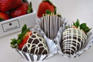 Picture of three chocolate covered strawberries with strawberries in the background.