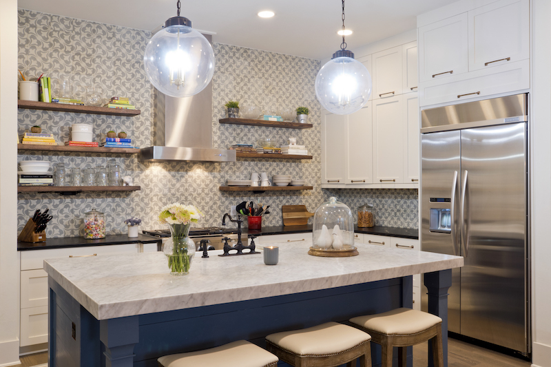 Carrera marble island counter anchors the light-filled kitchen where black soap stone countertops contrast with pale gray and white backsplash of hand made cement tiles reaching ceiling height. Stainless steel appliances, bronze and brass lighting fixtures, black farmhouse faucet and brass hardware that is hung horizontally on cabinets and drawers add panache. Stools are covered in Sunbrella fabric for kid- friendly use.